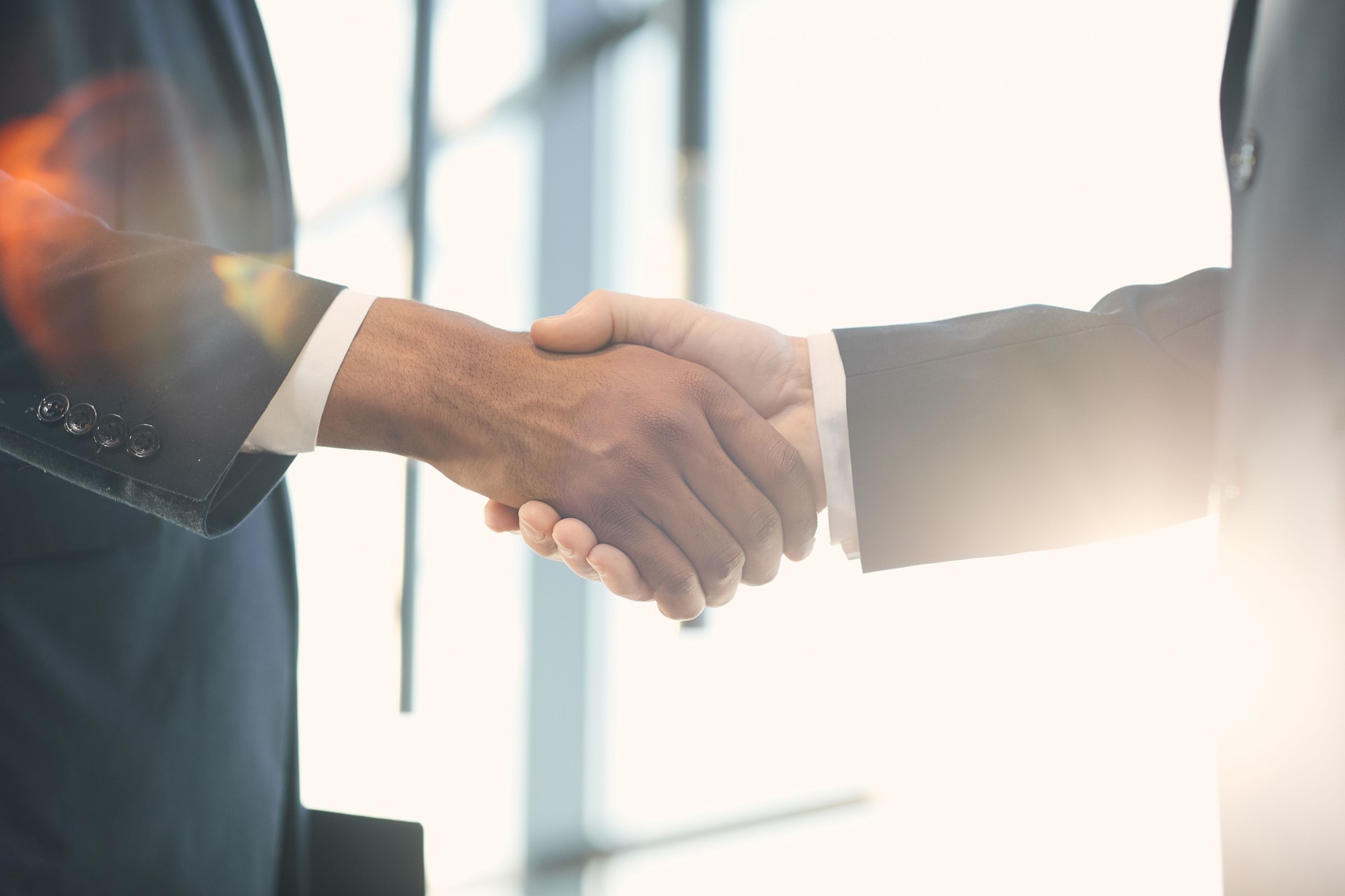 Close-up of unrecognizable multi-ethnic business partners in suits handshaking in light, gesture symbolizing trust and respect